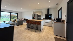 A modern kitchen with a central island, bar stools, and a dining area with a sofa and chairs. - Air-conditioned house, South Corsica, 4 bedrooms, 2 bathrooms, 15 min from the beach (Figari)