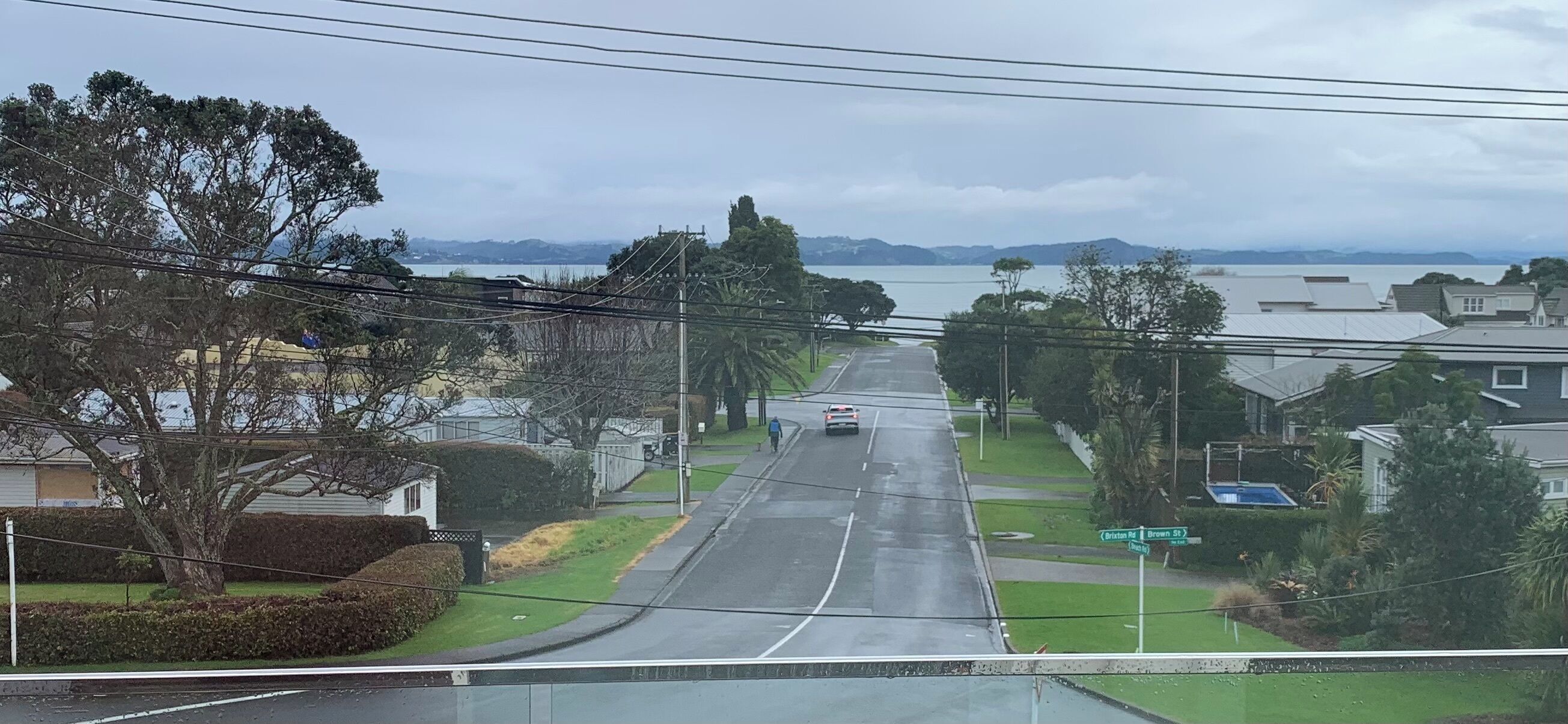 A residential street with houses, a road, and a body of water in the distance.