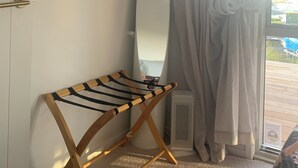 Habitació amb televisió penjada, un mirall gran, una cadira plegable de fusta i una finestra amb cortines.