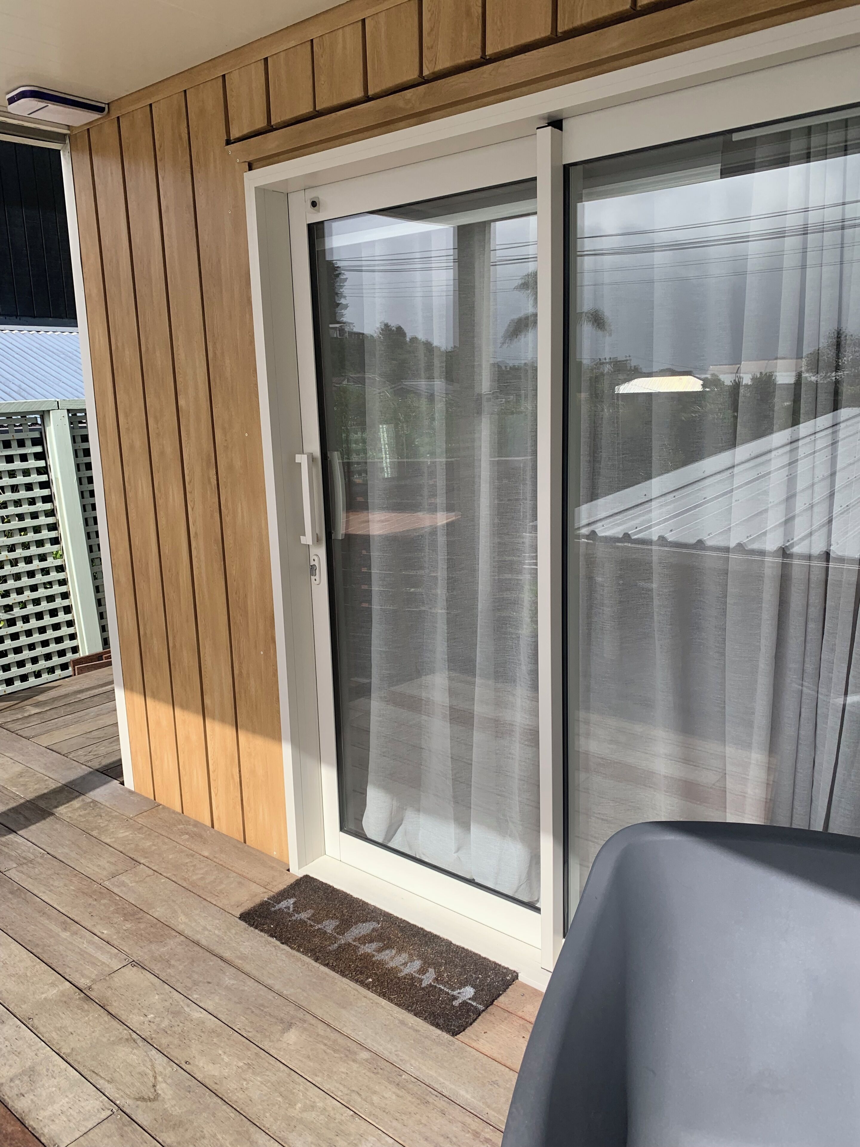 Puerta corrediza de vidrio que da a una terraza con piso de madera y felpudo.