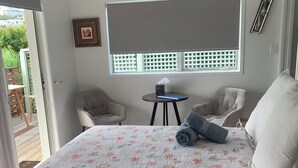 Een slaapkamer met een groot bed, twee stoelen, een tafeltje en een raam met uitzicht op groen.
