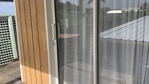 Een schuifdeur die uitkomt op een balkon met een houten terras en een deurmat.