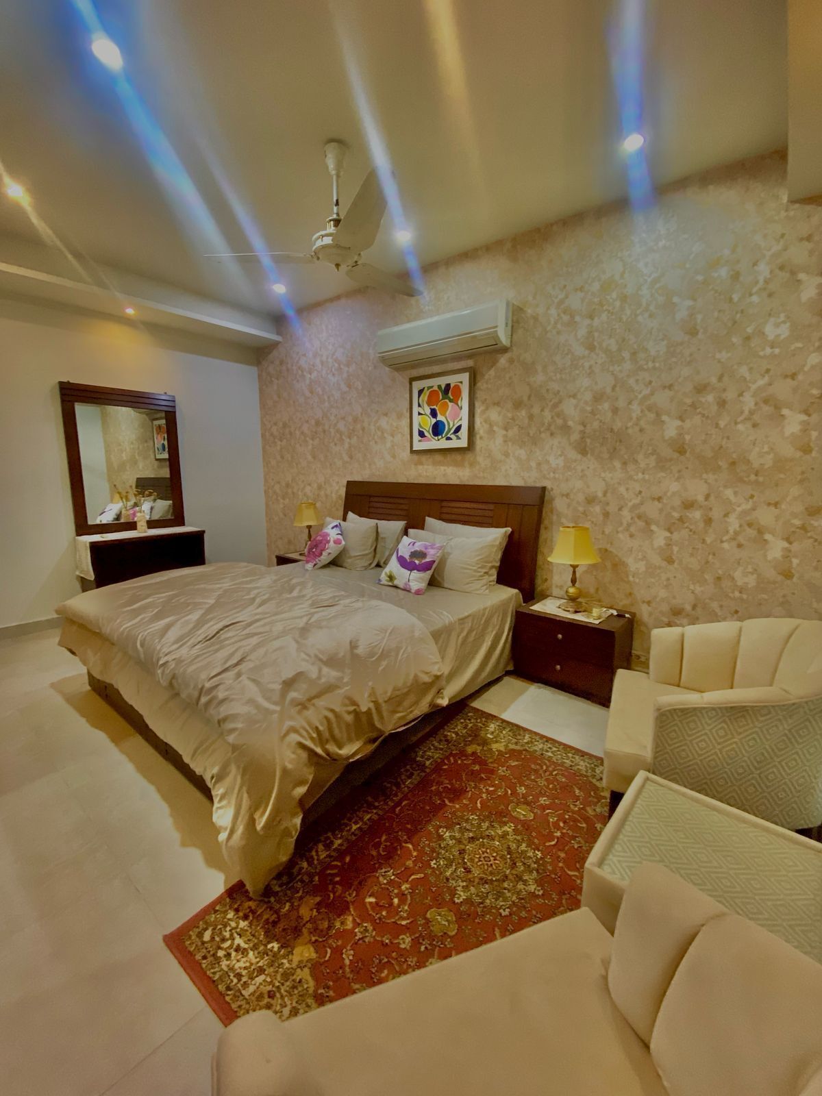 A bedroom with a bed, bedside tables, a chair, a mirror, and a ceiling fan.