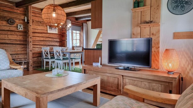 L’intérieur chaleureux d’un chalet avec une table à manger en bois, des chaises, un téléviseur et une lampe décorative.
