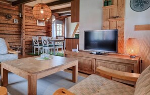 Interior acollidor d'una cabana amb taula de dinar de fusta, cadires, televisió i una làmpada decorativa.