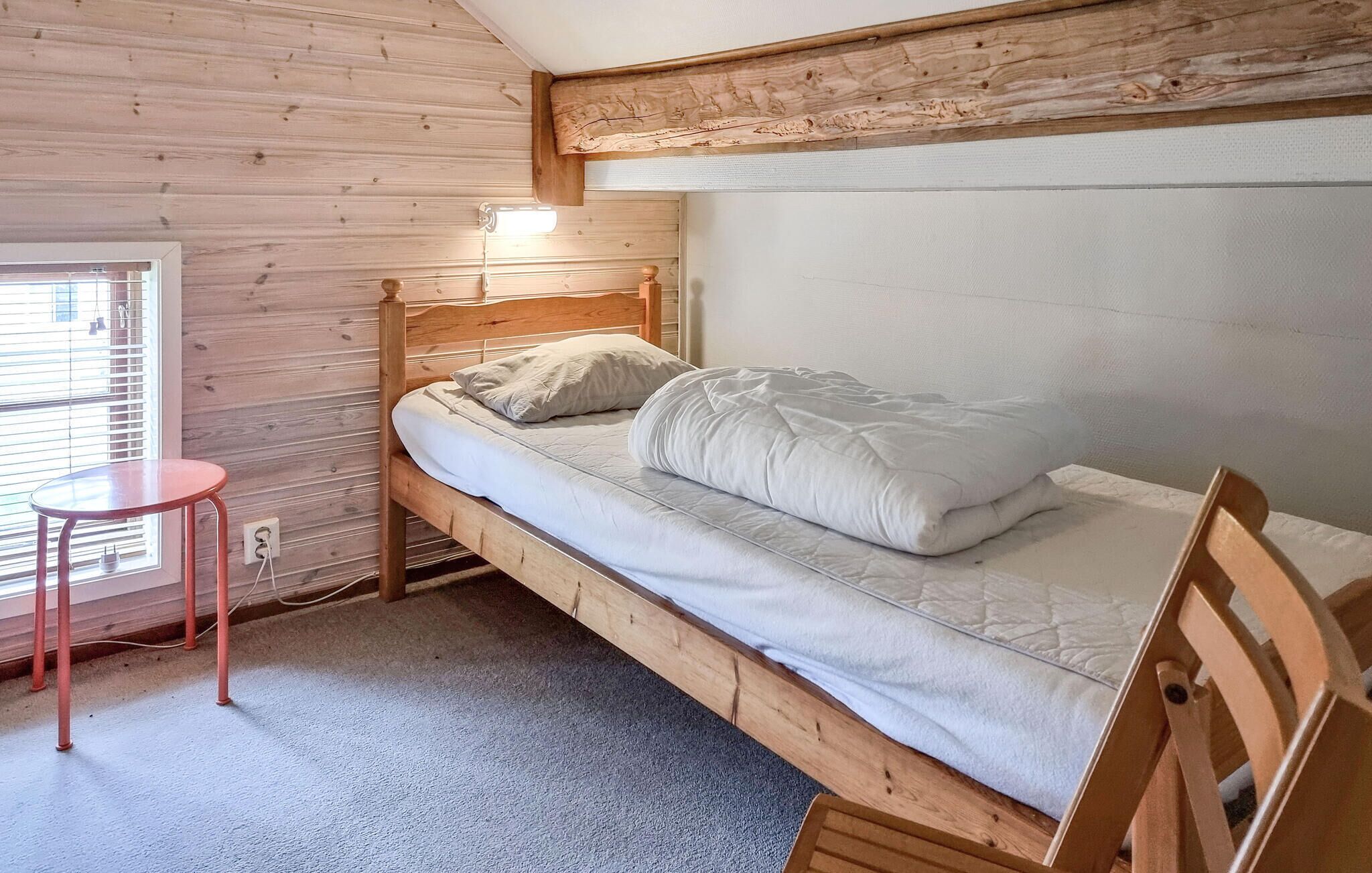 Ein Einzelbett mit Holzkopf, ein kleiner runder Tisch und ein Fenster mit Jalousien.