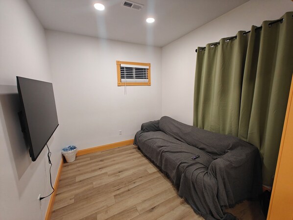 A small room with a sofa, a television mounted on the wall, a window with a wooden frame, and a curtain.