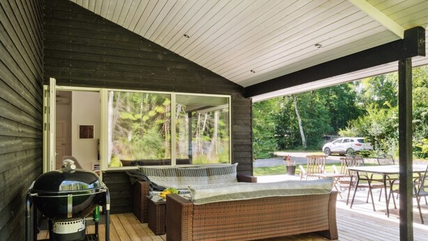 Une terrasse extérieure équipée d’un barbecue, de meubles en osier et offrant une vue sur la forêt environnante.