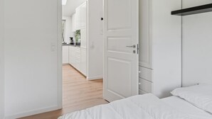 Une chambre à coucher avec un lit, une armoire blanche et une porte donnant sur la cuisine.