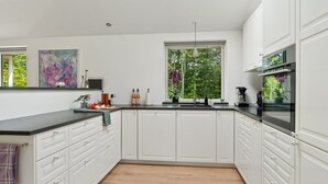 Une cuisine moderne avec des meubles blancs, un plan de travail noir et une grande fenêtre donnant sur un paysage verdoyant.