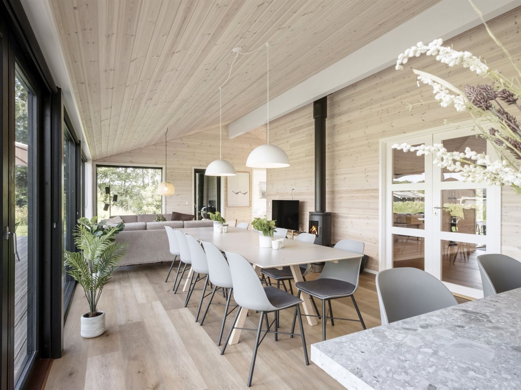 Un comedor moderno con una mesa larga, sillas, luces colgantes y una chimenea.