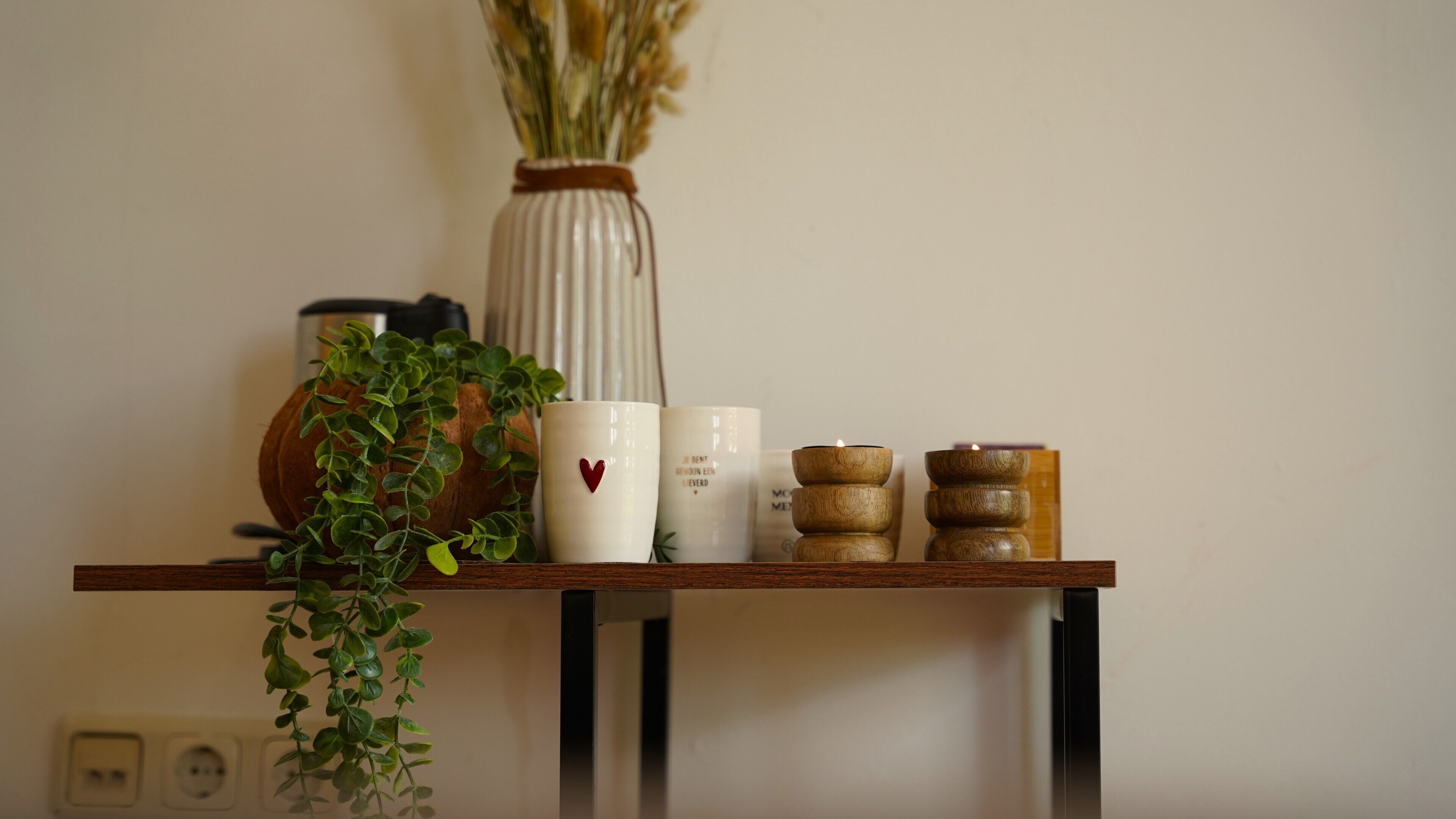 A wooden shelf with a vase, a potted plant, and several candles.