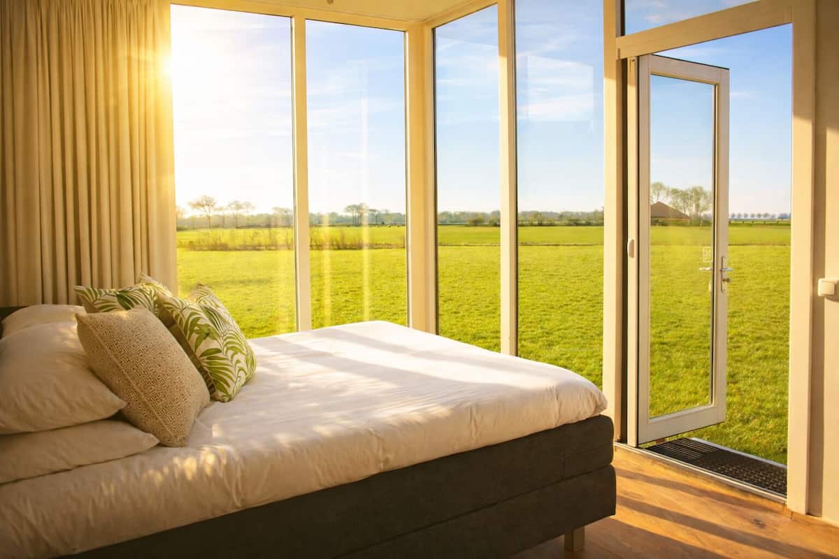 Ein Schlafzimmer mit einem großen Bett, Blick auf ein grünes Feld und einer Schiebetür.