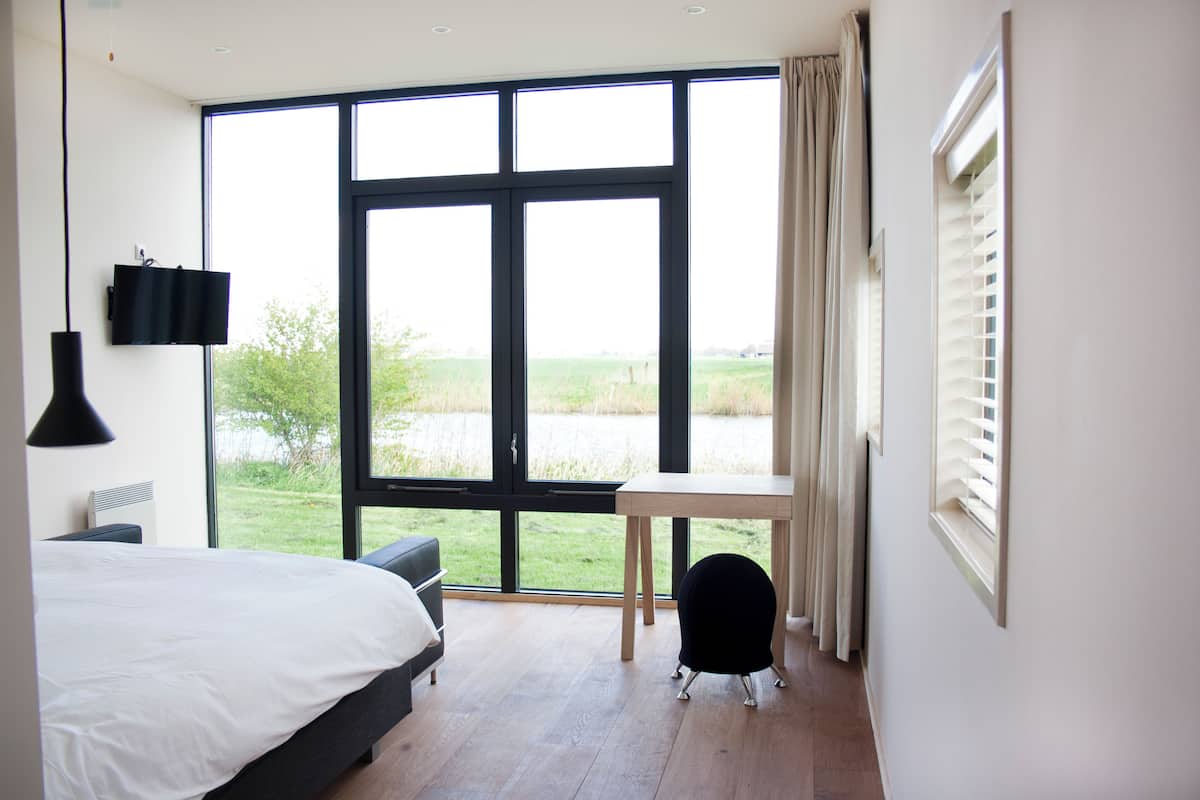 Ein Schlafzimmer mit großem Fenster, einem Bett, einem Schreibtisch und einem Sessel.