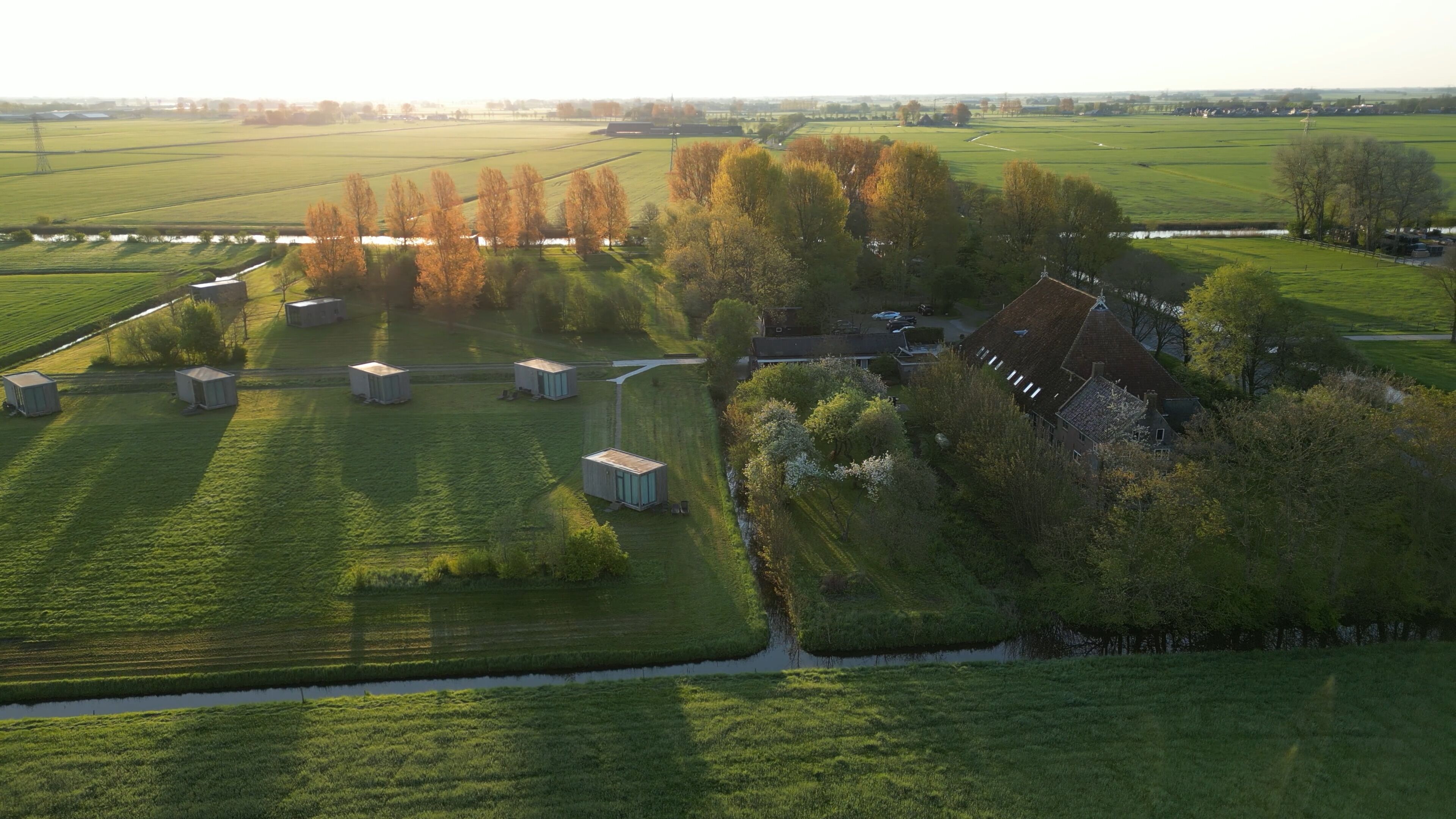 Een luchtbeeld van een landelijk gebied met groene velden, enkele gebouwen en een groot huis met een hellend dak.