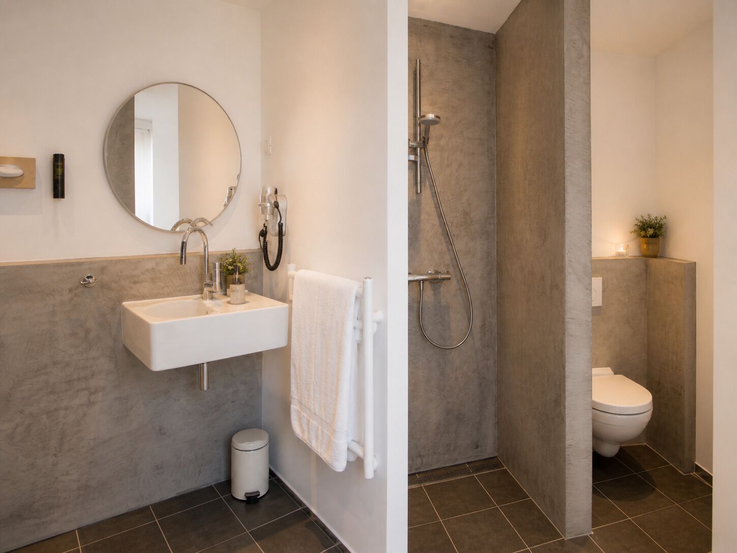 Ein modernes Badezimmer mit Waschbecken, Spiegel, Handtuchhalter, Dusche und Toilette.