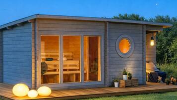 Una pequeña cabaña de madera de un piso con un porche, ventanas grandes y un tragaluz circular.