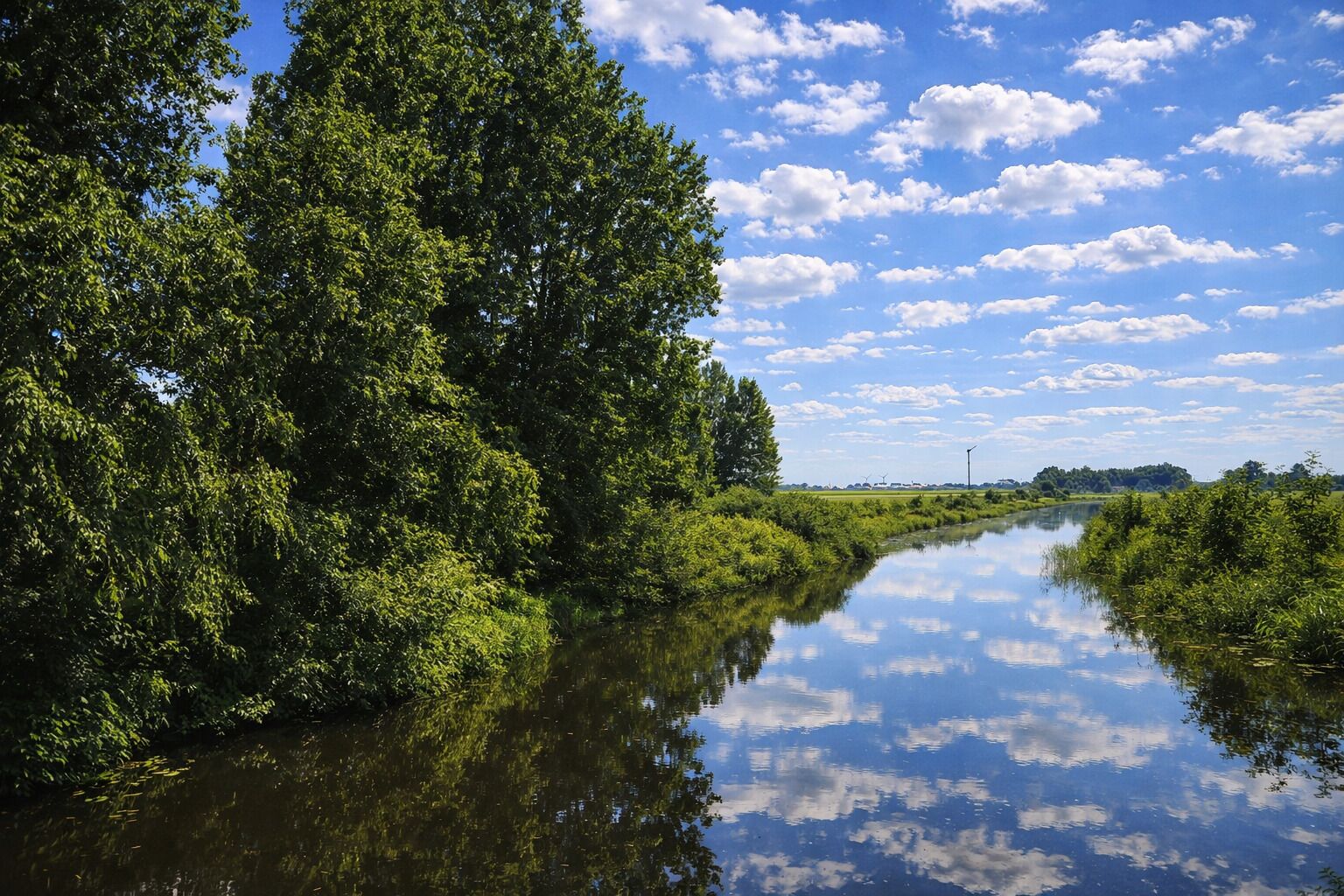 A calm river flanked by dense green foliage under a partly cloudy sky.