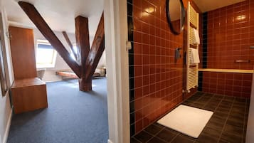 Ein Zimmer mit freiliegenden Holzbalken, einer Bank, einer Fliesenwand, einem Spiegel und einem Handtuchhalter.