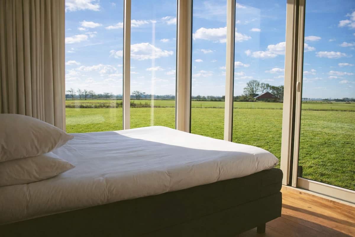 Ein Schlafzimmer mit einem großen Bett, Blick auf ein grünes Feld und einem klaren Himmel.