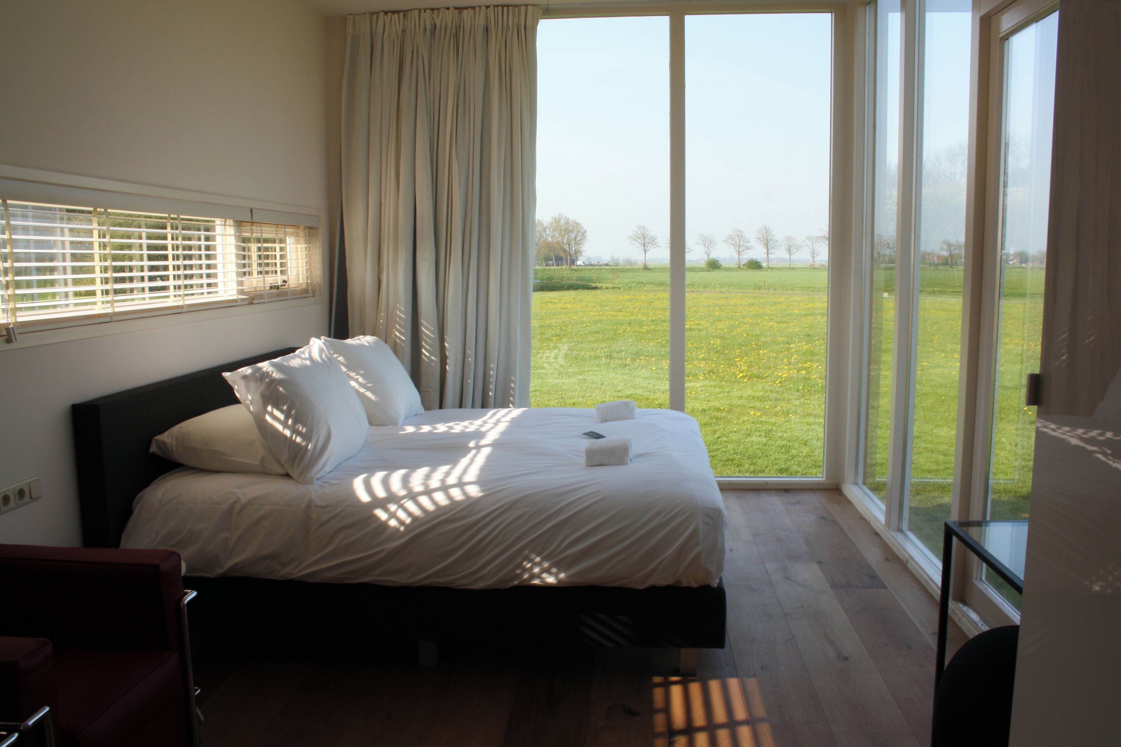 A bedroom with a large bed, a view of a grassy field, and a window with blinds.