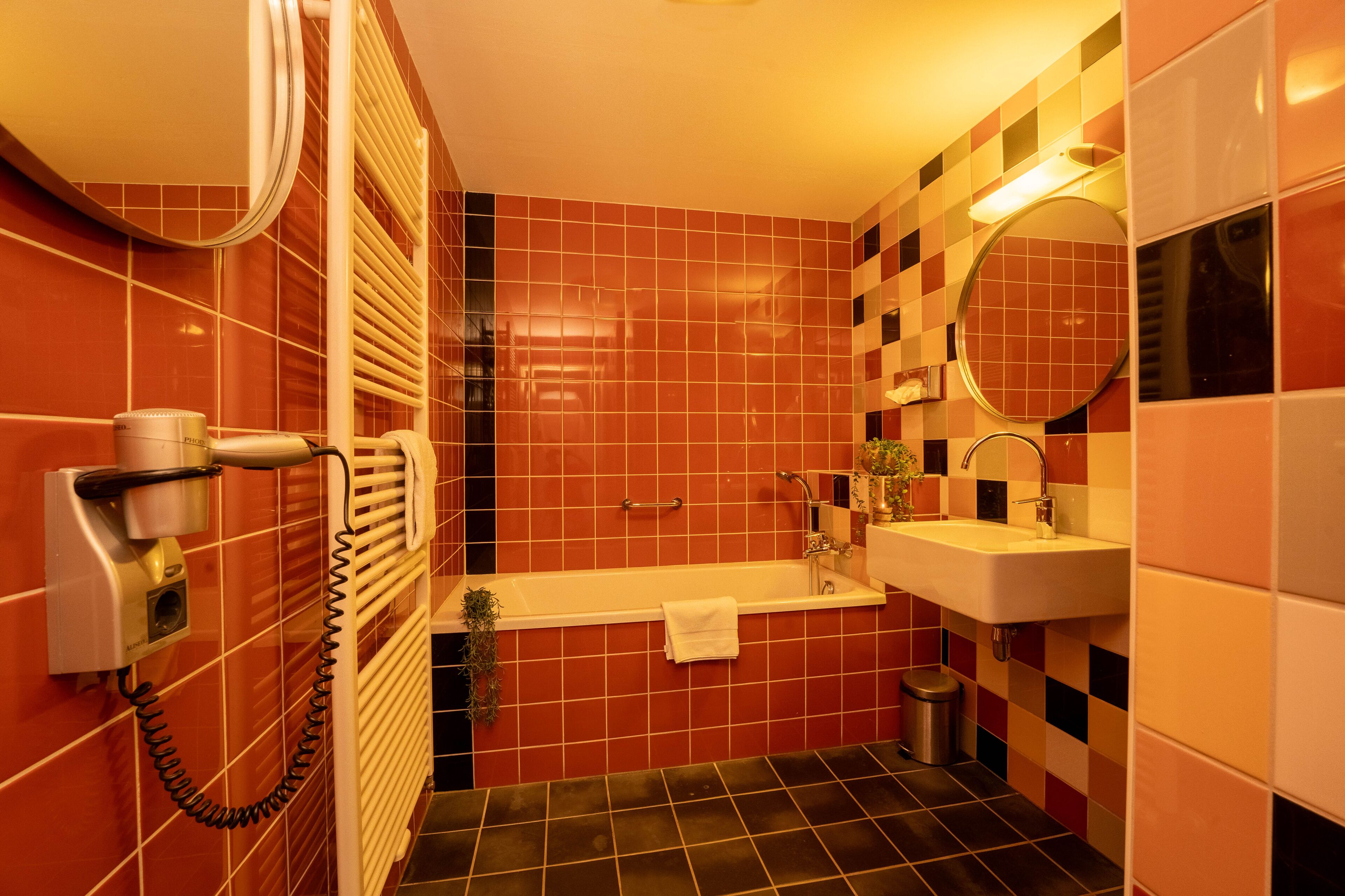 Une salle de bain avec des carreaux de sol rouges et noirs formant un motif à carreaux, une baignoire blanche, un lavabo et un miroir.