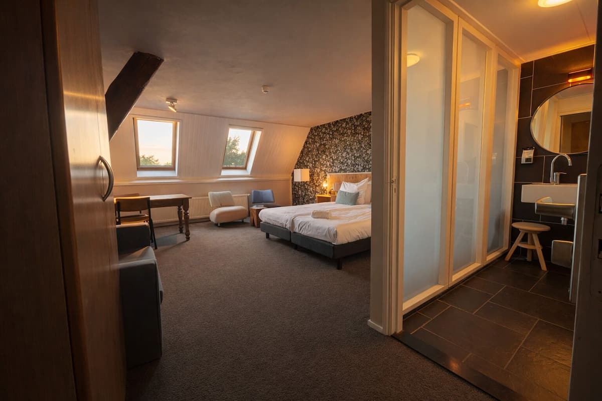 Ein Schlafzimmer mit Bett, Schreibtisch, Stuhl, einem kleinen Tisch und einem Badezimmer mit Waschbecken und Spiegel.