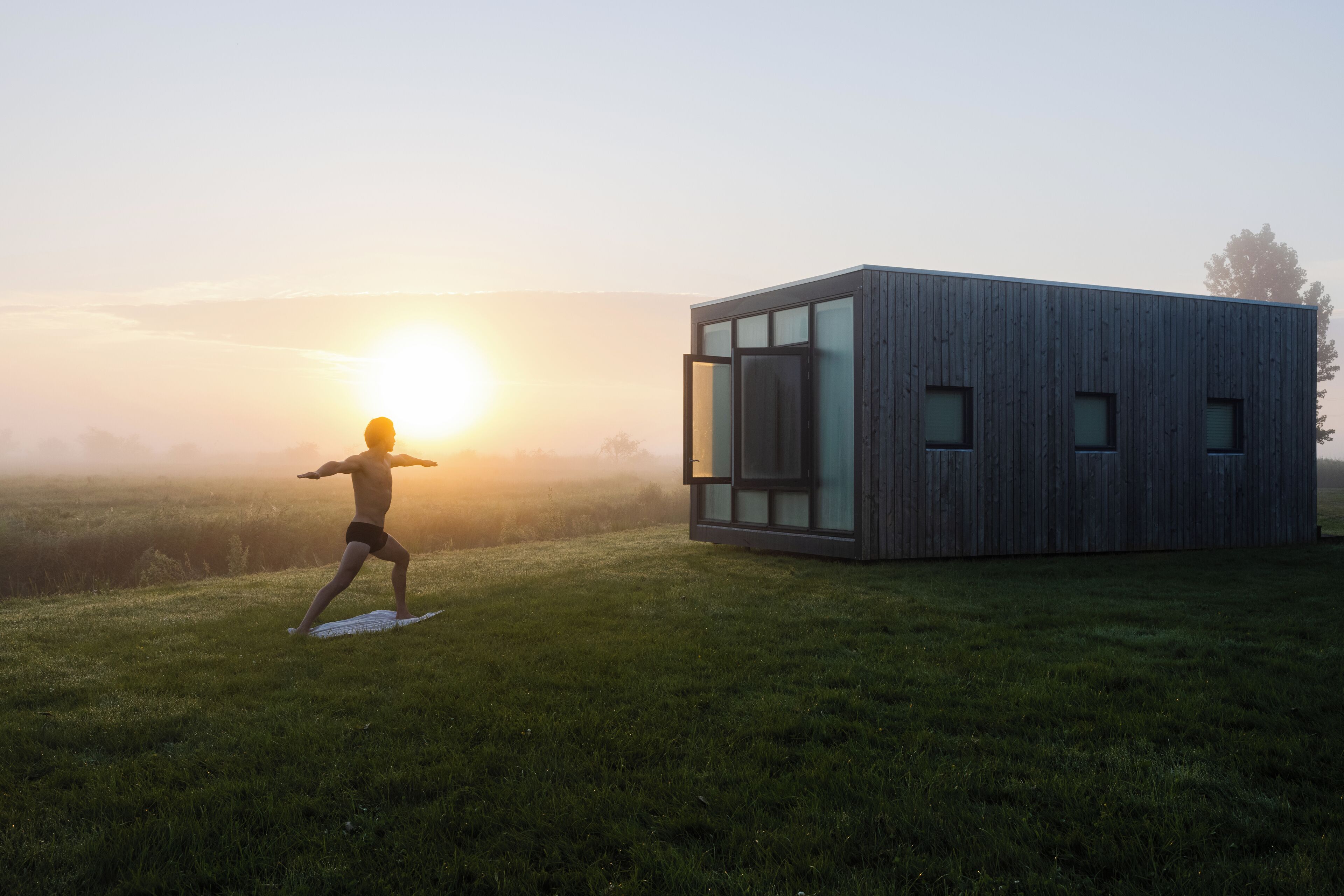 A modern building with large windows and a person practicing yoga on a grassy field.