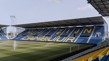 A stadium with blue and yellow seating, a roof structure, and a visible scoreboard.