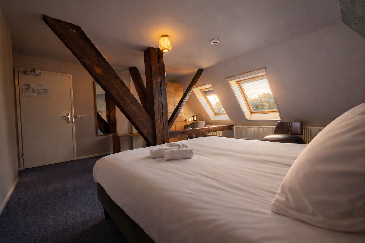A bedroom with a large bed, a desk, a chair, a radiator, and a window.