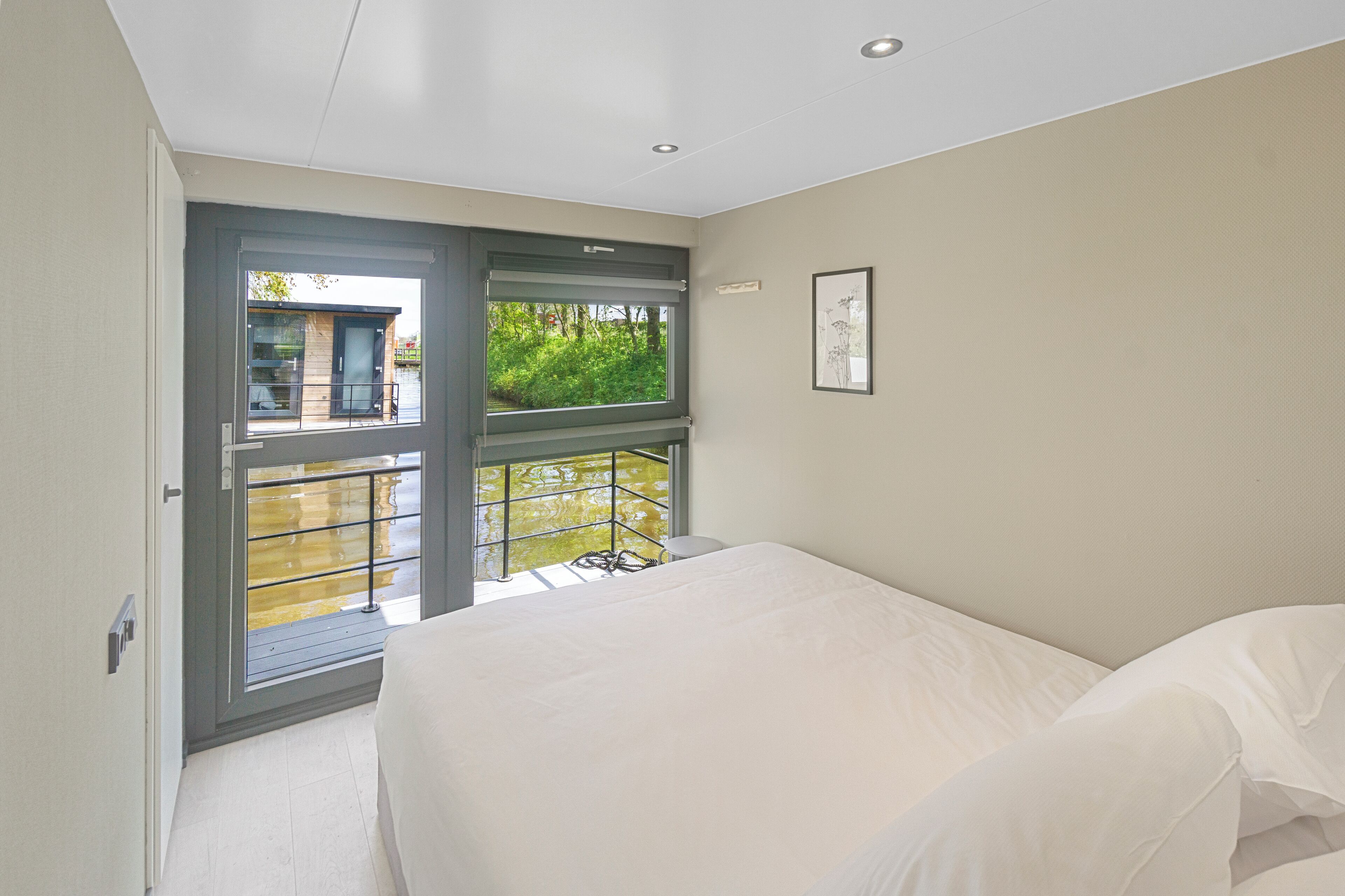 A bedroom with a large bed, a window with a view of greenery, and a balcony.