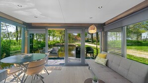 A modern interior with a dining area, a sofa, and large windows offering a view of a garden and a pond. - Pean-buiten Weidum (Weidum)