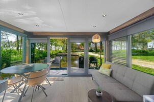 Ein modernes Interieur mit Essbereich, einer Couch und großen Fenstern mit Blick auf einen Garten und einen Teich.