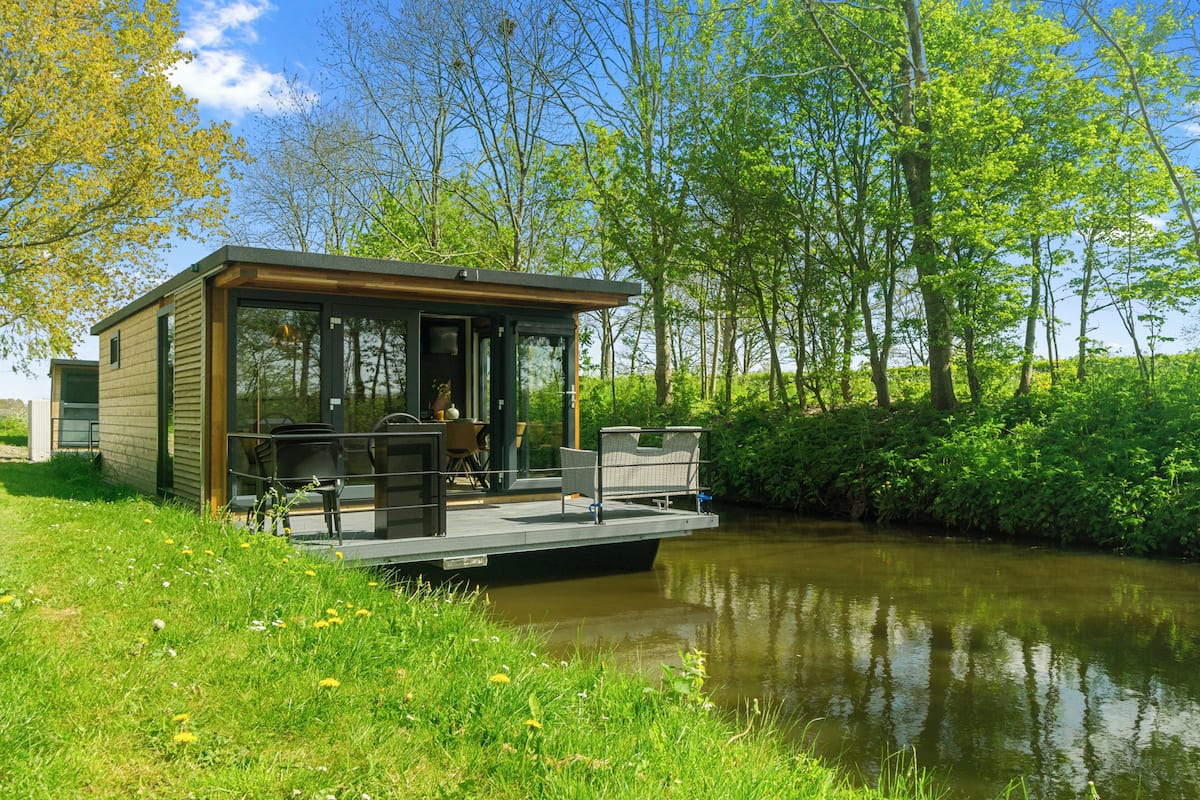 Ein modernes Hausboot mit Deck, Sitzgelegenheiten und einer Glasveranda.