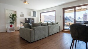 A modern living room with a grey sofa, a potted plant, and a dining area with a chair.