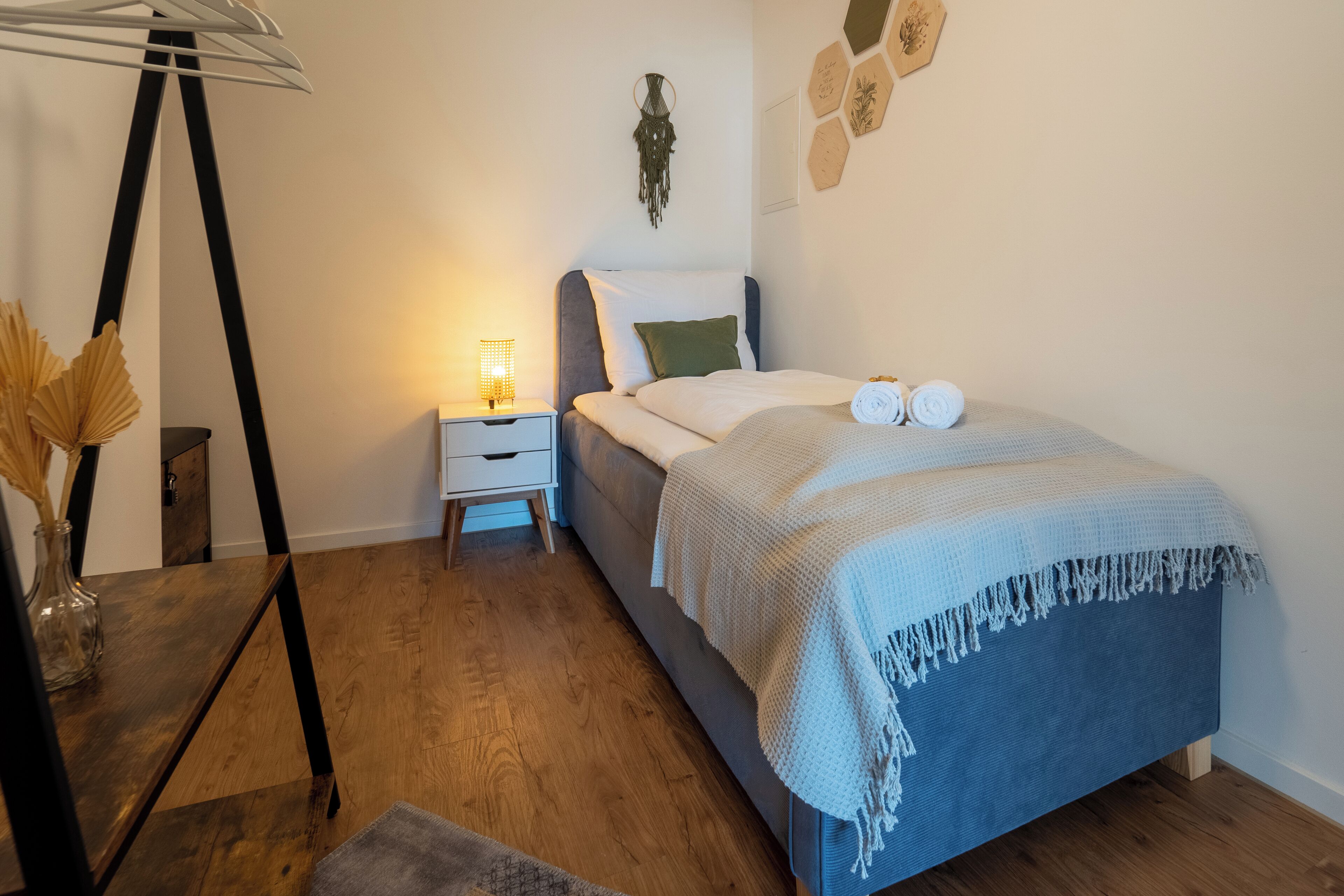 Un dormitorio con cama, mesita de noche, lámpara y decoración en la pared.