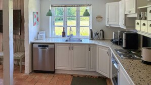 Cocina con armarios blancos, lavavajillas, ventana con vista a follaje y encimera con varios electrodomésticos.