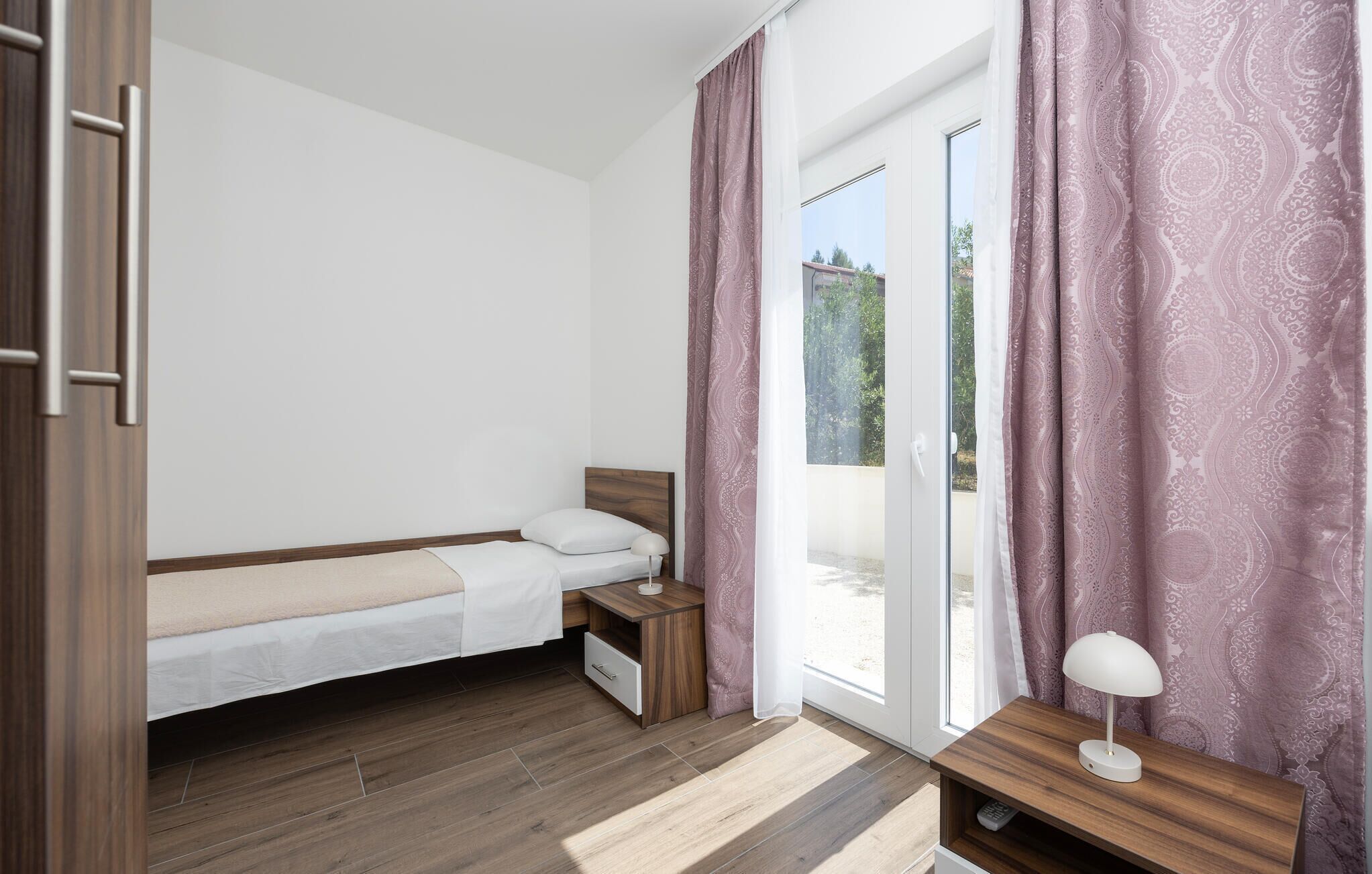 Un dormitorio con cama, mesita de noche y escritorio con lámpara.