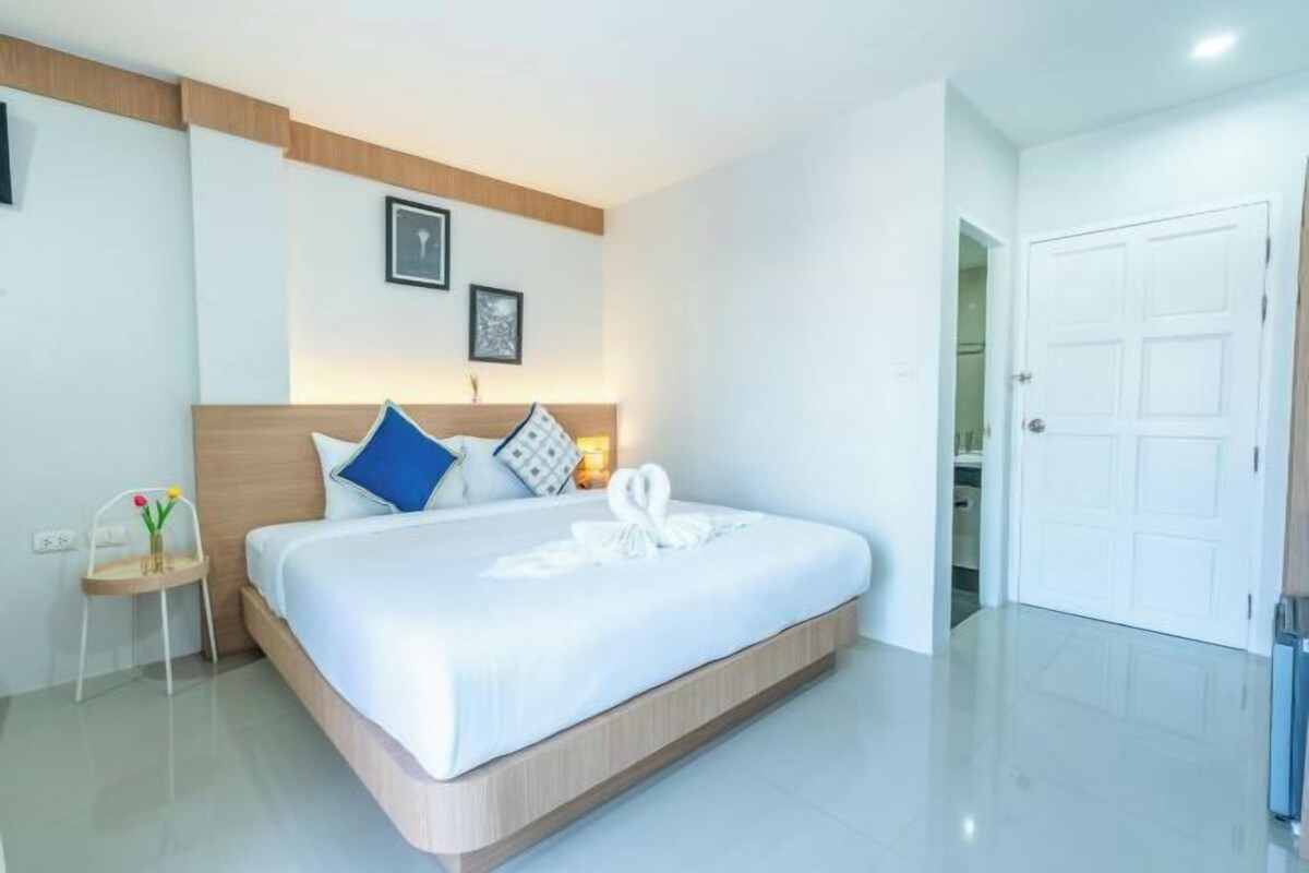 A modern hotel room with a large bed, a bedside table with a vase of flowers, and a door leading to a bathroom.