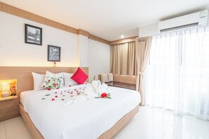 A hotel room with a large bed, a bedside table with a lamp, a window with curtains, and an air conditioning unit. - Seaside Patong House (Patong)