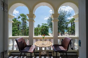 Un balcon doté de trois arcades, de deux chaises, d’une table ronde et d’un vase rempli de fleurs.