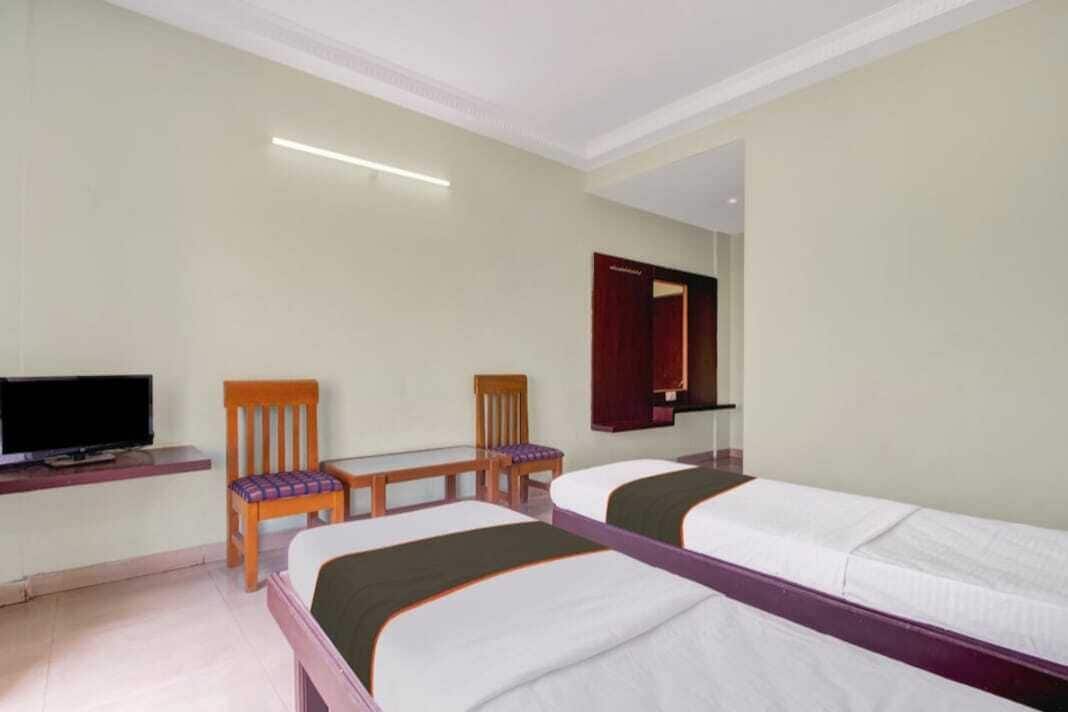 Habitación de hotel con dos camas individuales, televisión, escritorio y una silla.