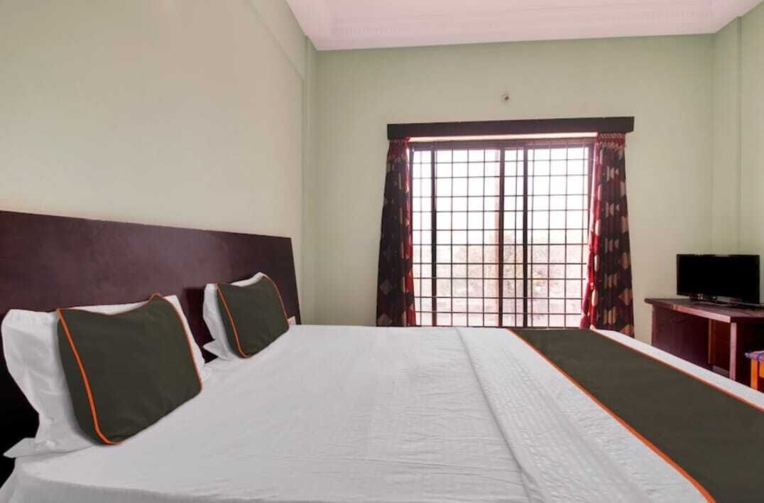 Habitación de hotel con una cama grande, un televisor sobre un mueble y una ventana con cortinas.