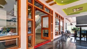 Un vestíbulo de hotel con una escalera, puertas de vidrio con marco de madera y una zona de estar con sillas.