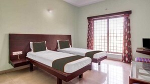 Habitación de hotel con dos camas individuales, televisión y ventana con cortinas.