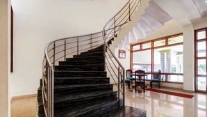 Una escalera curva con escalones de mármol negro y barandales de metal, que conduce a una habitación con amplios ventanales y una alfombra roja.