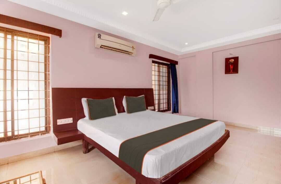 A bedroom with a large bed, an air conditioning unit, and a window with bars.