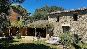 Ein Steinhaus mit einer Terrasse, einem kleinen Garten und einer mit Weinreben bewachsenen Pergola.