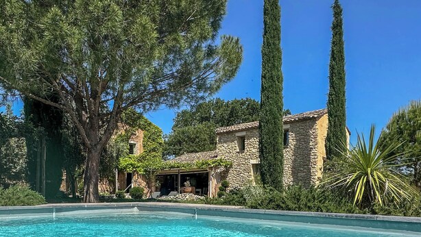 Blick über den Pool auf ein Steinhaus bei strahlend blauem Himmel.
