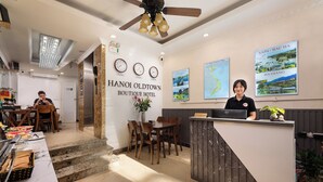 A reception area with a wooden reception desk, a seating area with chairs, a dining table with food, and a wall with clocks and a map. - Hanoi Oldtown Boutique Hotel  (Hanoi)